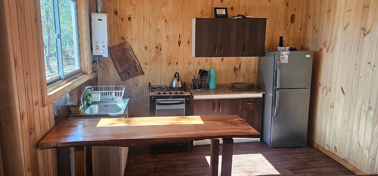 Cocina con mesa de madera nativa, cocina a gas y refrigerador