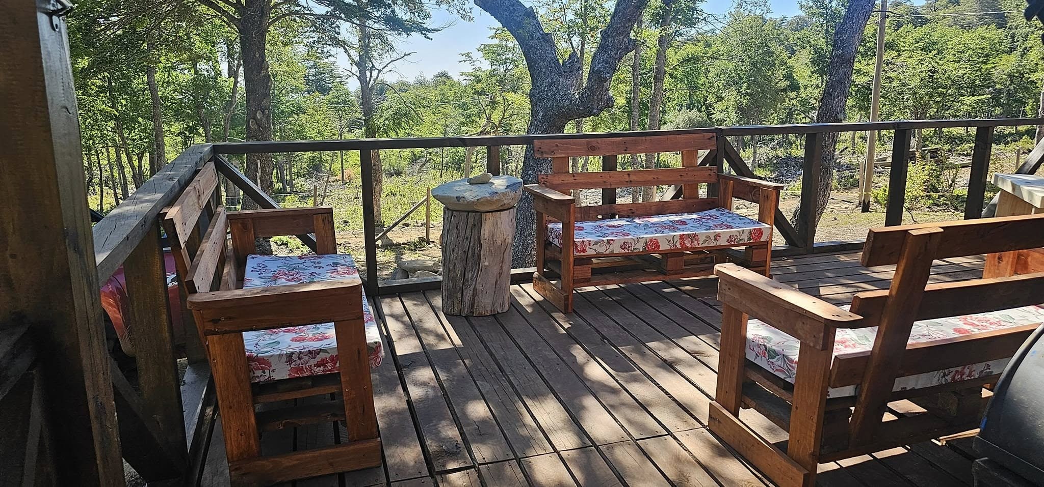 Terraza de madera con bancas y sillones hechos a mano mirando el bosque
