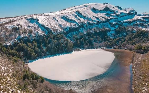 Vista aérea de la laguna congelada en invierno, bajo un cerro nevado